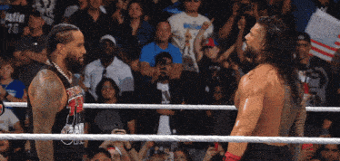 two men in a wrestling ring one of whom is wearing a shirt that says ' roman reigns ' on it
