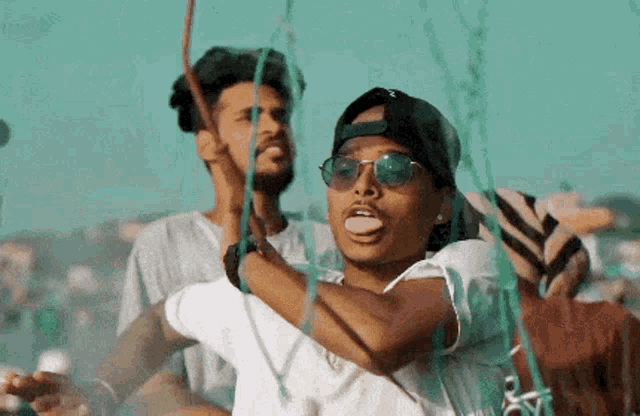 a man wearing sunglasses is sticking out his tongue while another man holds a rope .
