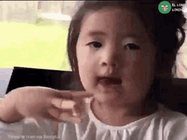 a little girl is making a funny face and pointing at her face .