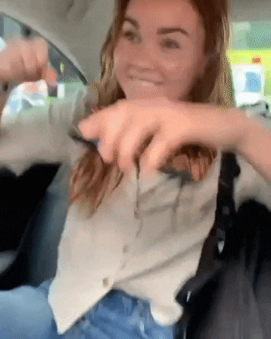 a woman is sitting in the back seat of a car cutting her hair with a knife .
