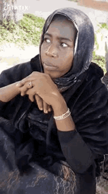 a woman wearing a hijab is sitting on a bench with her hands folded and looking at the camera .