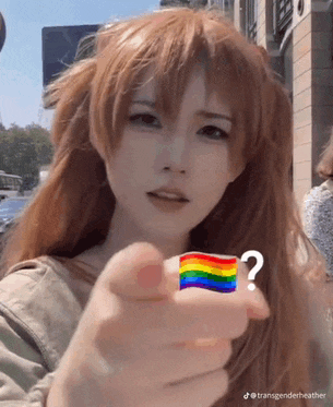 a woman is pointing at a rainbow flag and has a question mark on her finger .