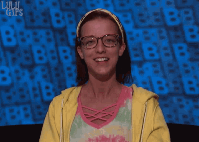 a girl wearing glasses and a headband is smiling in front of a lulu gif