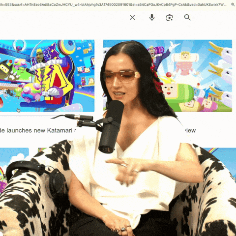 a woman is sitting in a chair with a microphone in front of a screen that says " launches new katamari "