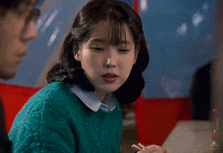 a woman in a green sweater is sitting at a table with chopsticks and a man .