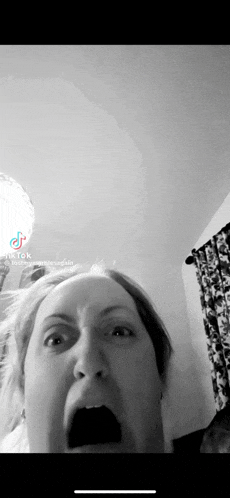 a black and white photo of a woman making a funny face with her mouth open .