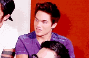 a young man in a purple shirt is sitting next to another young man