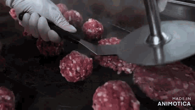 a person holding a spatula over a bunch of meatballs with the words made in animotica on the bottom