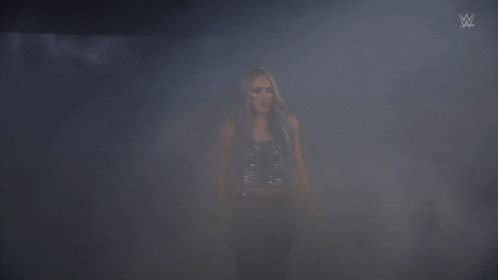 a woman with blue hair is standing in a dark room with a wwe logo on the wall