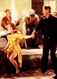 a woman in a yellow dress is dancing with a man in a black shirt .