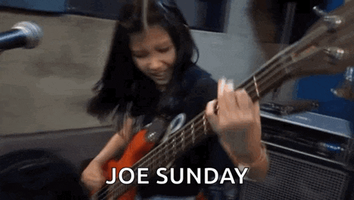 a young girl is playing a bass guitar in front of a microphone and the words joe sunday are visible .