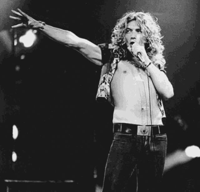 a shirtless man singing into a microphone with his arm outstretched