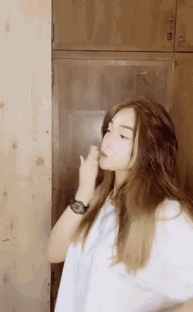 a woman with long hair is standing in front of a wooden cabinet .