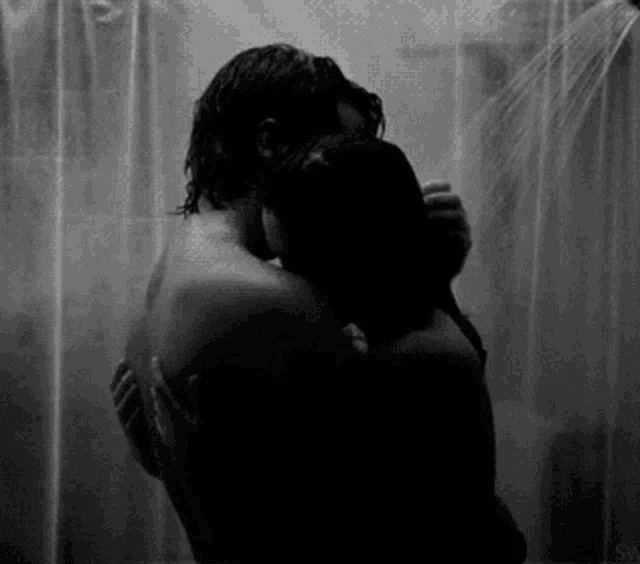 a black and white photo of a man and woman hugging in the shower .