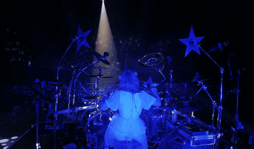 a woman in a white dress is playing drums in a dark room with blue lights