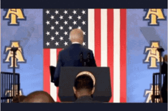 a man stands at a podium in front of a flag