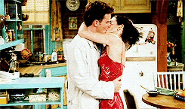 a man and a woman kissing in a kitchen with a fridge in the background