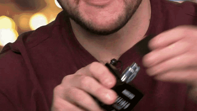 a man in a maroon shirt is opening a bottle of armani