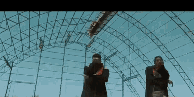 two men are standing in front of a large metal structure with a blue sky in the background