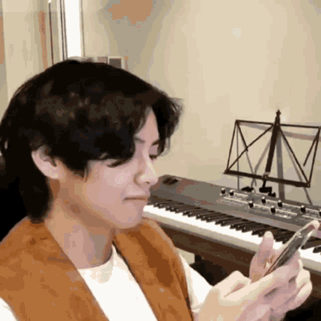 a young man is sitting at a piano looking at his phone .