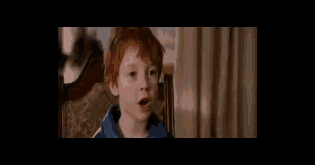 a young boy with red hair is sitting in a chair and talking to someone .