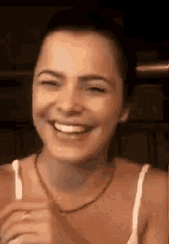 a woman is smiling with her eyes closed and wearing a white tank top and a necklace .