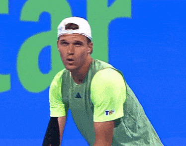 a man wearing a green adidas shirt and white hat