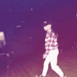 a person wearing a plaid shirt and white pants is dancing on a wooden floor .