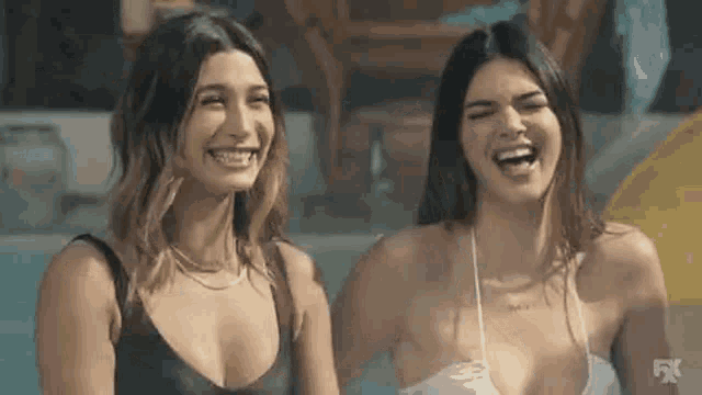 two women in bikinis are sitting next to each other in a pool and laughing .