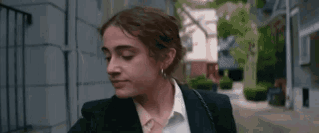 a woman in a black suit and white shirt is walking down a sidewalk .