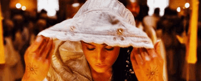 a woman wearing a white hat is covering her head with a white cloth .