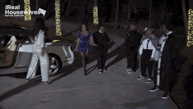 a group of people standing in front of a car that says real housewives on the bottom
