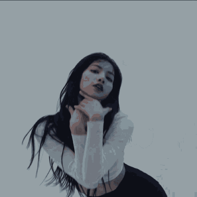 a woman in a white crop top and black shorts is dancing in front of a white wall .