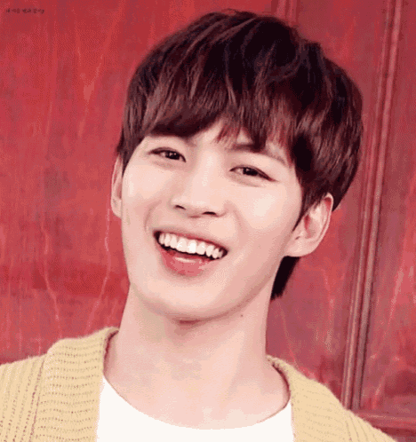 a young man wearing a yellow cardigan and a white shirt is smiling with his mouth open .