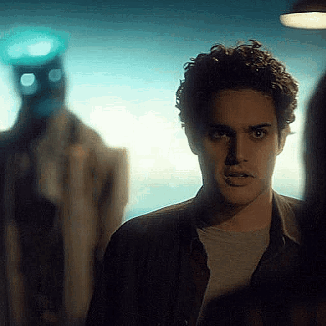 a man with curly hair is standing in front of a statue with a mask on his face .