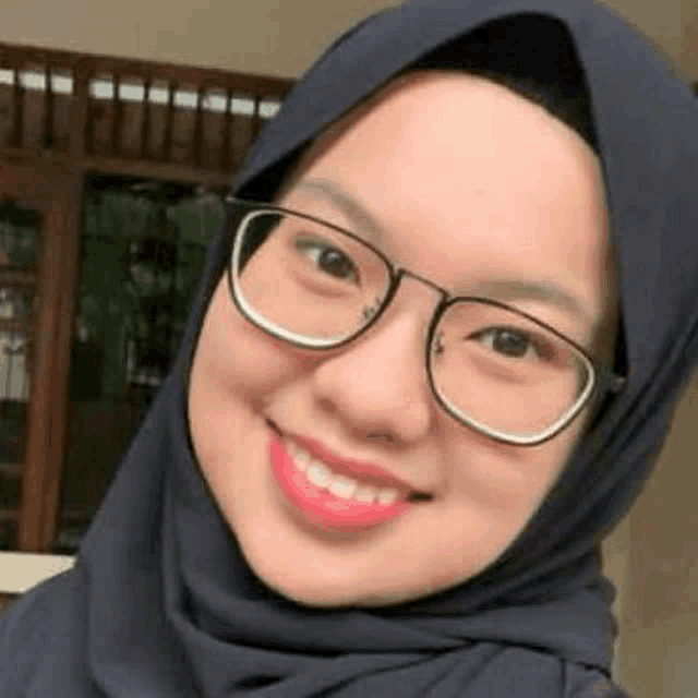 a close up of a woman wearing a hijab and glasses smiling .