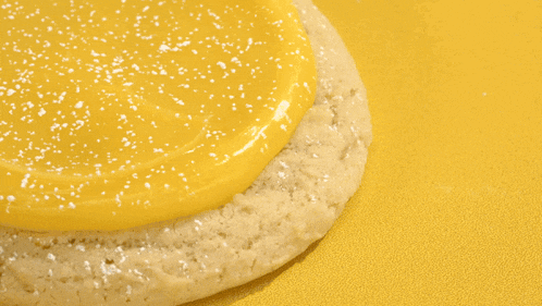 a person in black gloves is spreading yellow frosting on a cookie