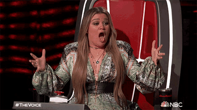 a woman is sitting in a chair with her mouth open and a sign that says the voice on it