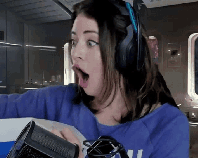 a woman wearing headphones and a blue shirt with the letter u on it looks surprised