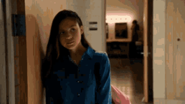 a girl in a blue shirt is standing in a hallway next to a wooden door .