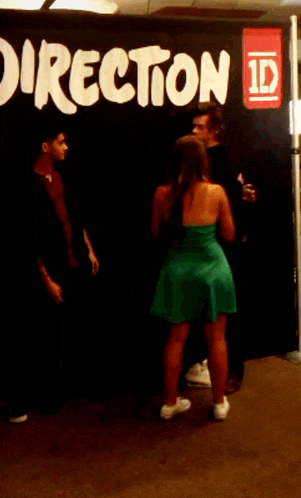 a woman in a green dress is standing in front of a direction sign