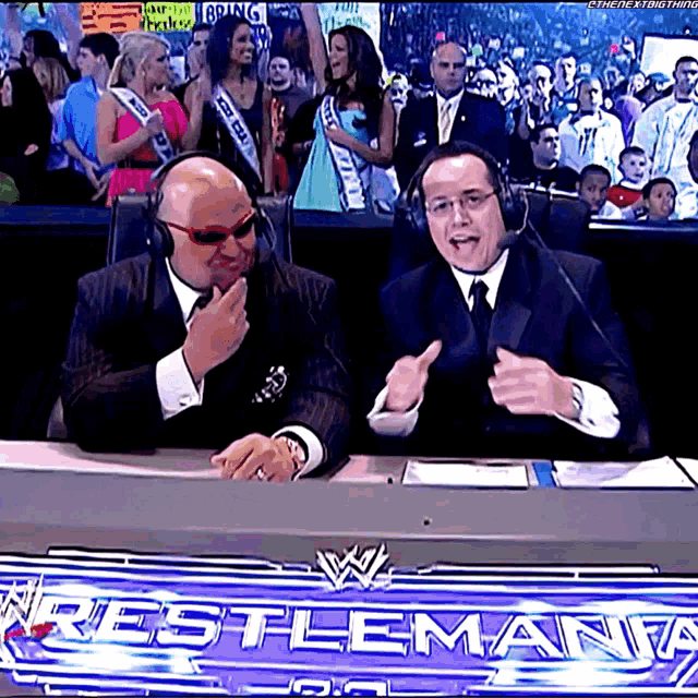 two men sitting in front of a wrestlemania sign