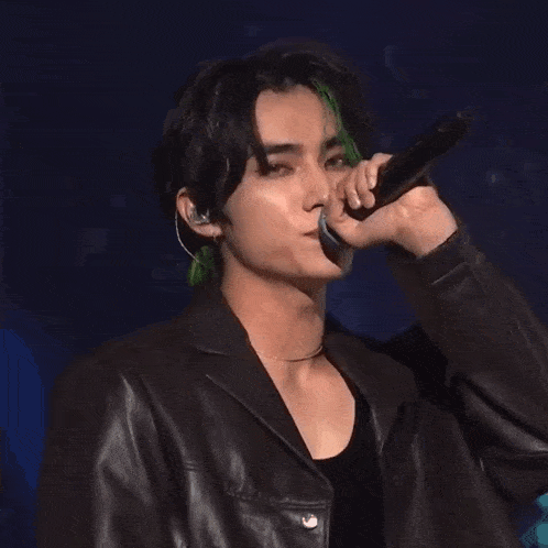 a man with green hair is singing into a microphone while wearing a leather jacket