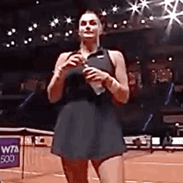 a woman in a black dress is standing on a tennis court holding a tennis racket .