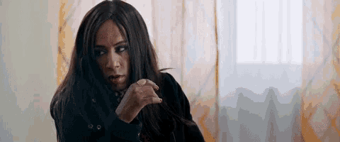 a woman with long hair and a ring on her finger is sitting in front of a window