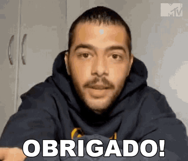 a man with a beard is wearing a hoodie and says obrigado