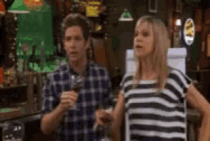 a man and a woman are standing next to each other in a bar . the woman is wearing a striped shirt .