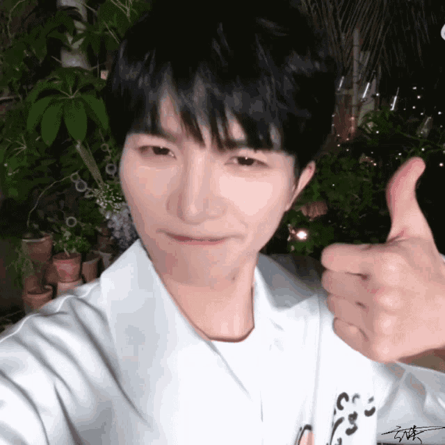 a young man giving a thumbs up in front of some potted plants