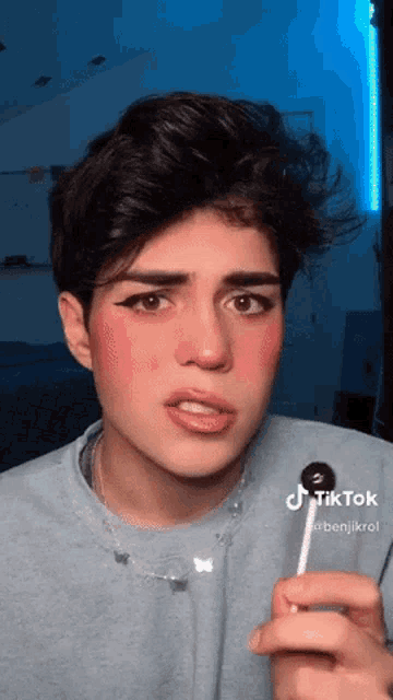 a young man with makeup on his face is holding a lollipop in his hand ..