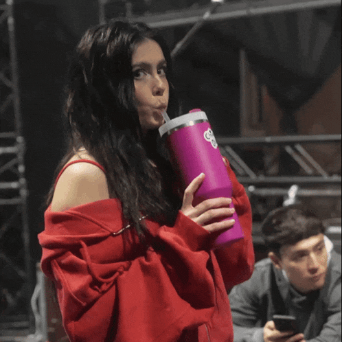a woman in a red shirt is drinking from a purple bottle